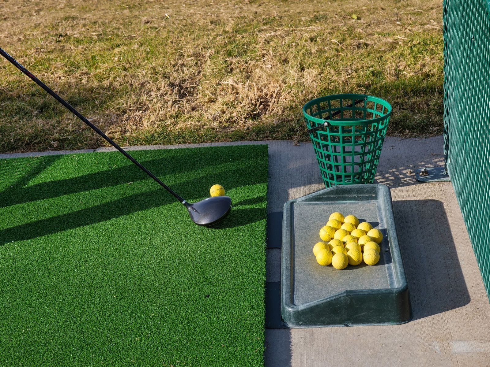 A driving-range hitting mat with a golf club and yellow balls