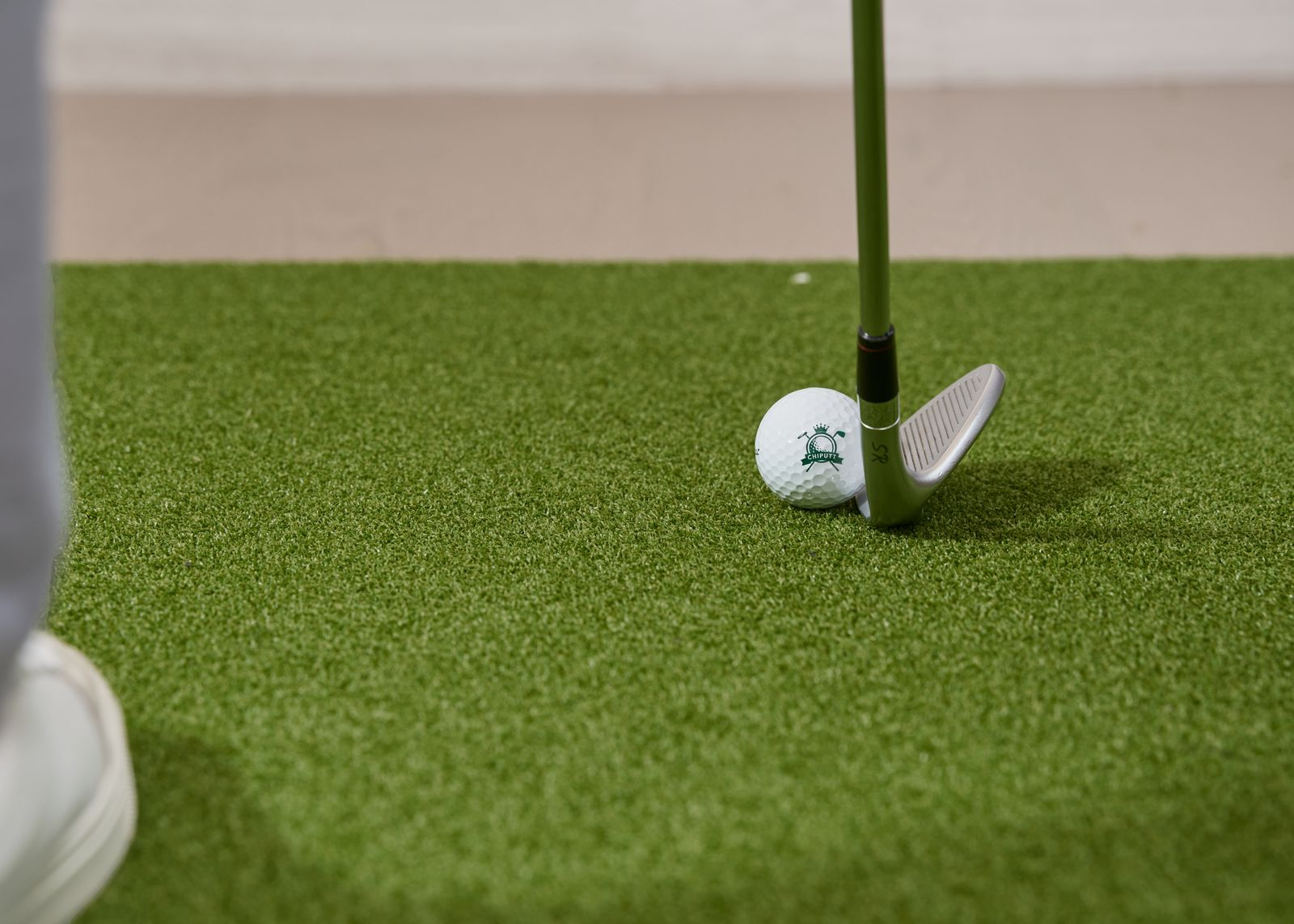 Close-up of a golf club and ball resting on artificial turf