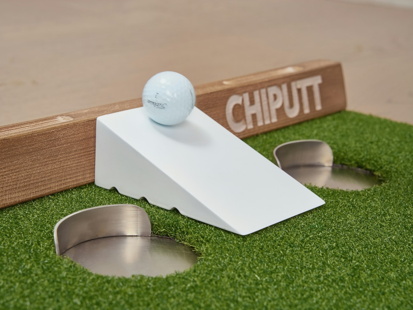 A golf ball on a ramp near putting holes on turf