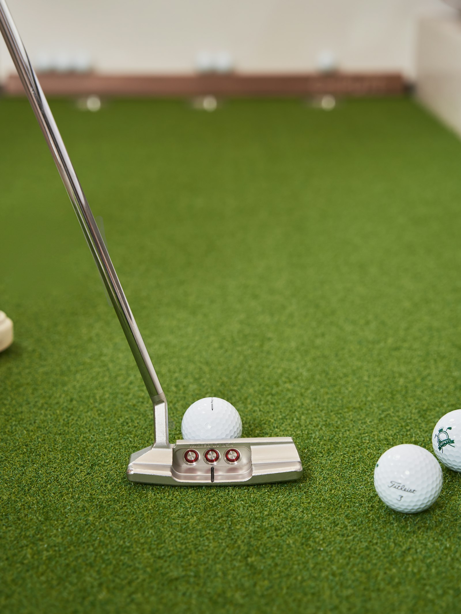 A putter with several golf balls resting on green artificial turf
