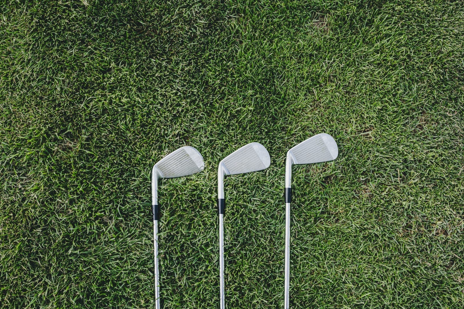 Three golf clubs laid out on green turf