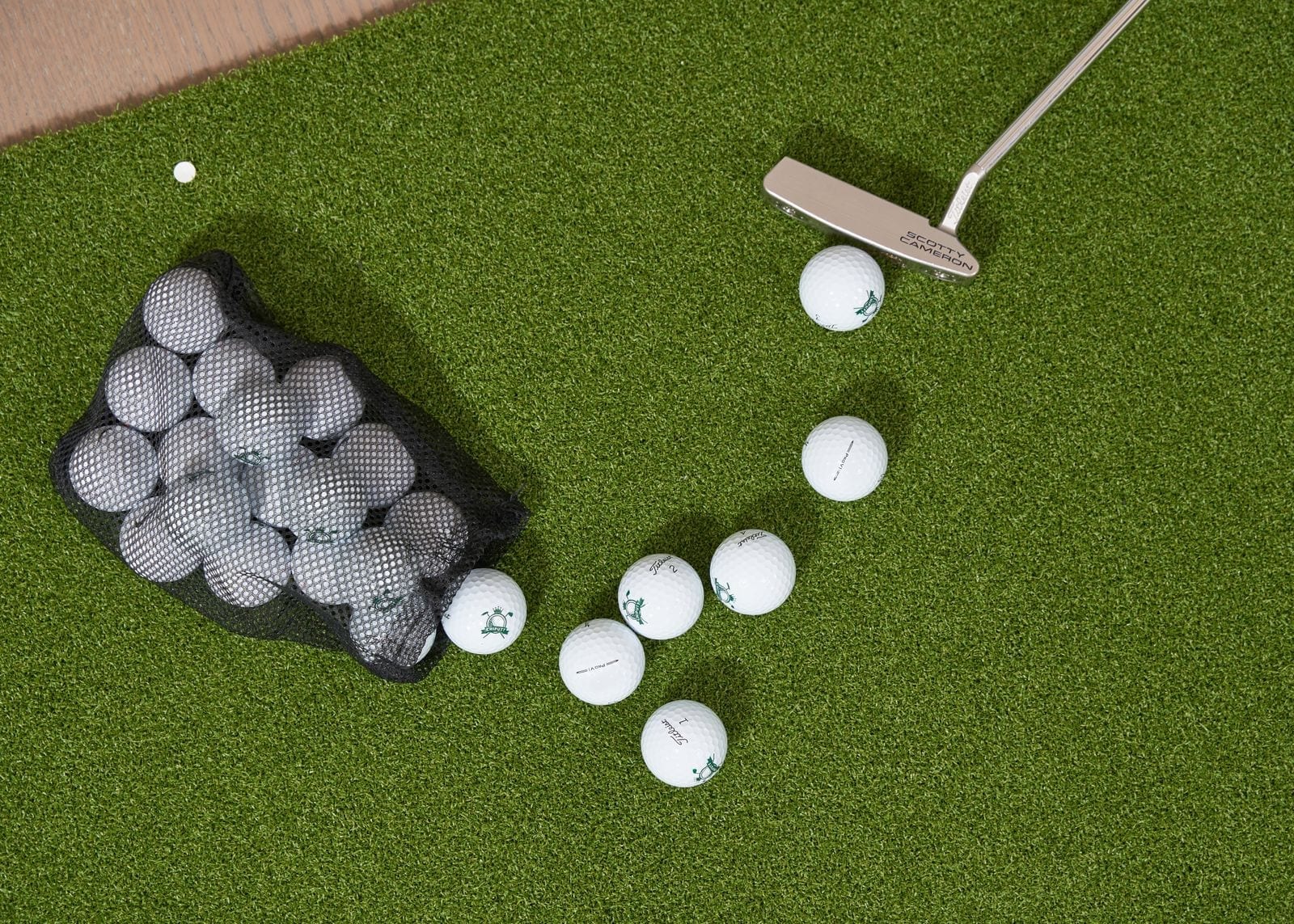 Golf balls, a putter, and a golf bag arranged on artificial putting-green turf