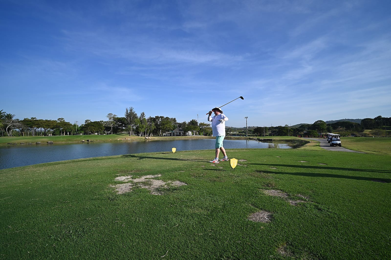 A golfer following through on a driver tee shot beside a water hazard
