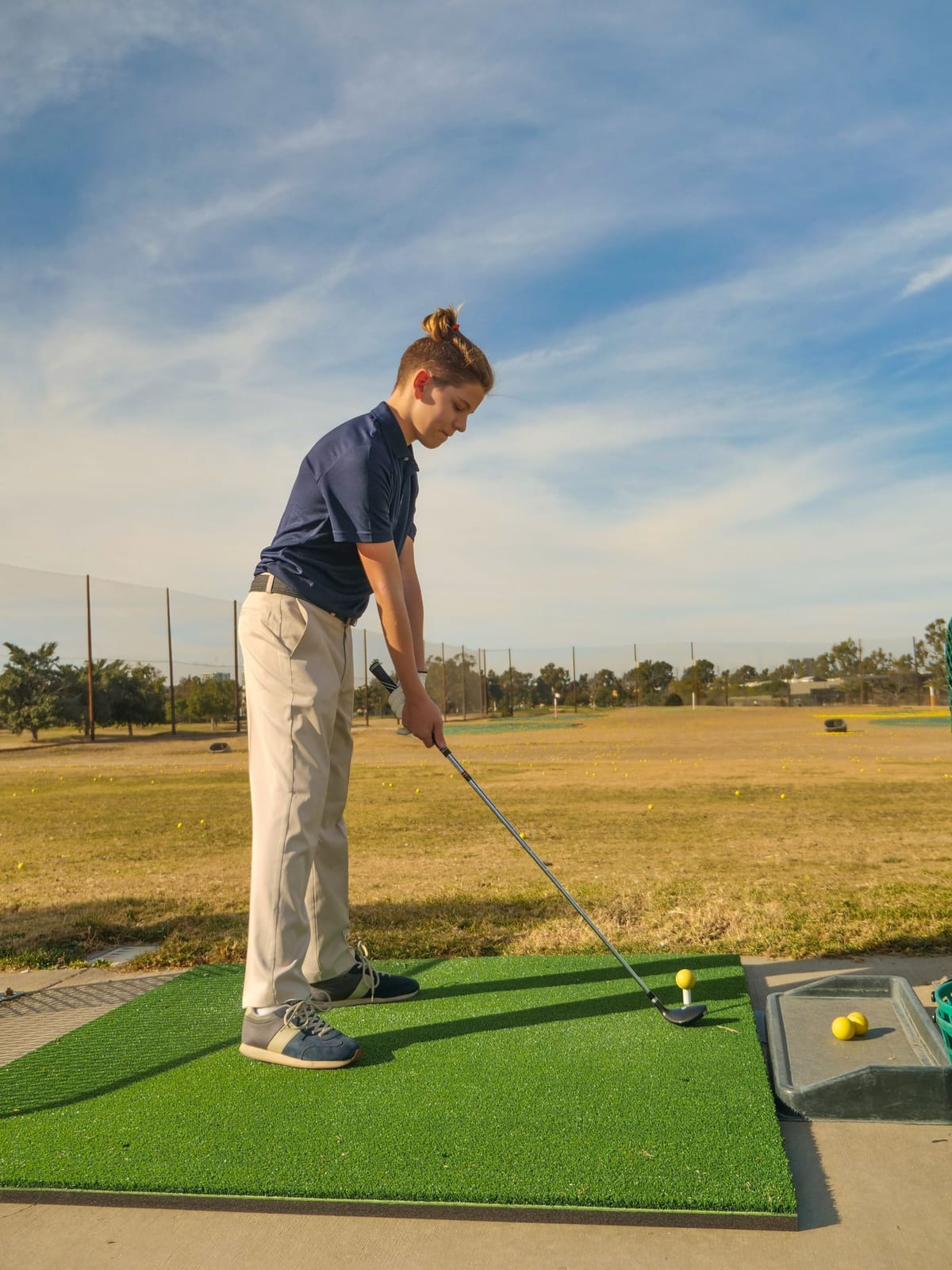 A golfer at address over a ball on a single hitting mat