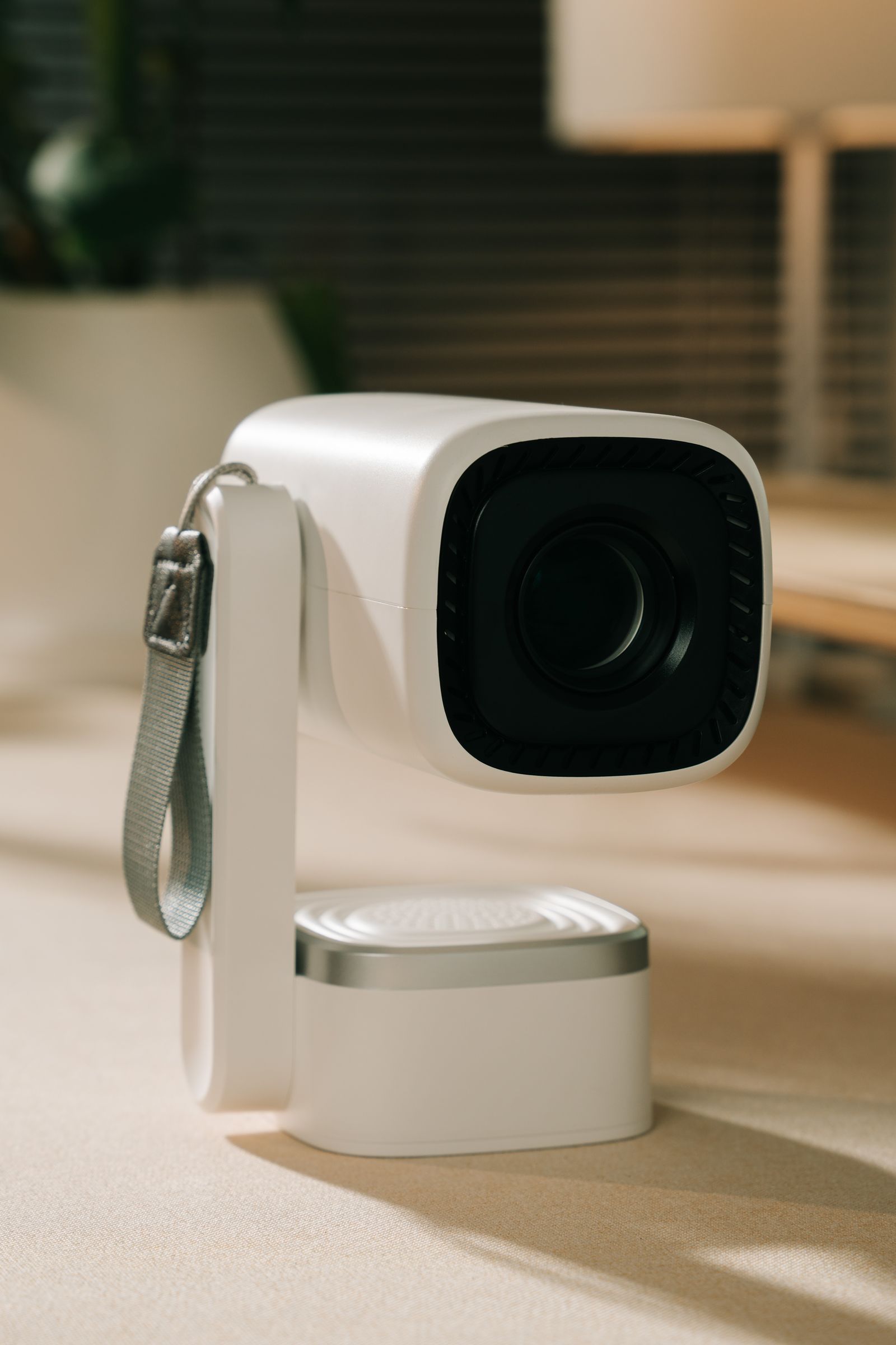 A compact white projector on a pivoting base, lens toward the camera, on a neutral tabletop.
