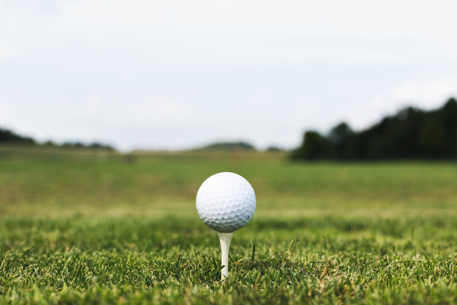 A white golf ball resting on a wooden tee in the grass