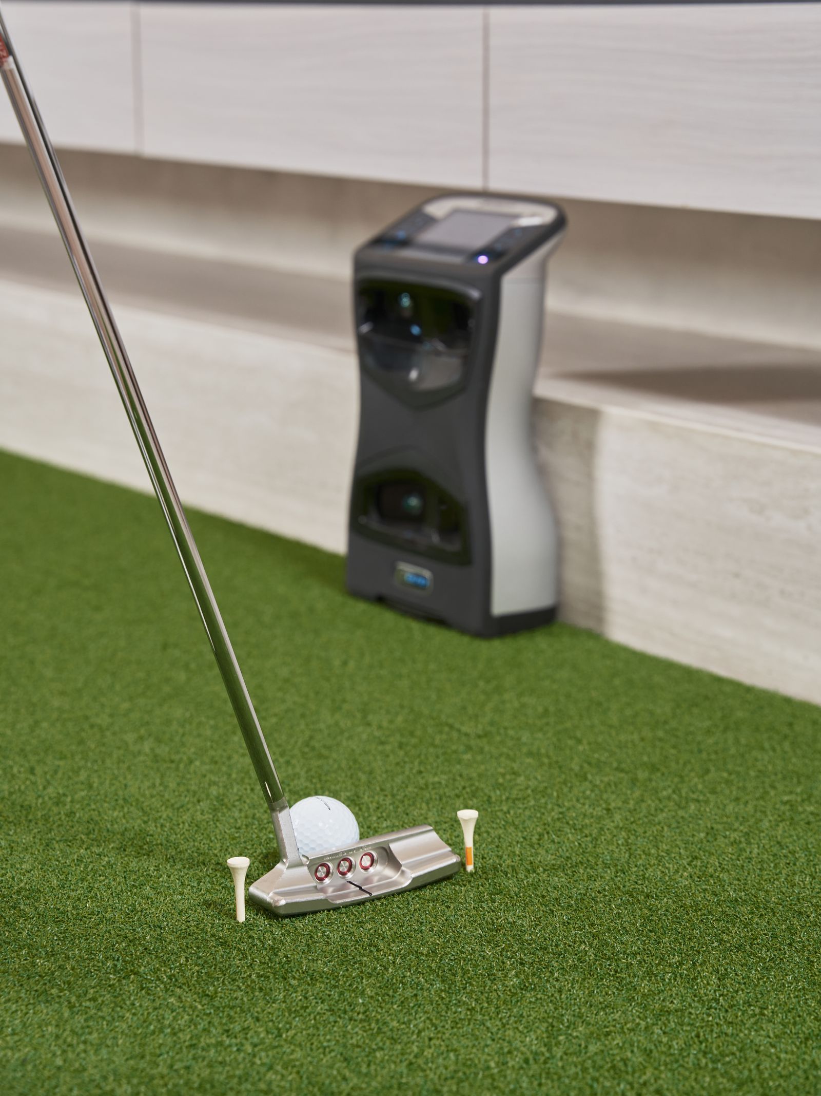 Indoor golf practice on artificial turf with a putter and a tracking sensor nearby