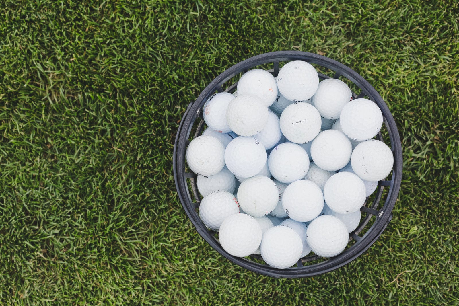 A basket of white golf balls on a driving range